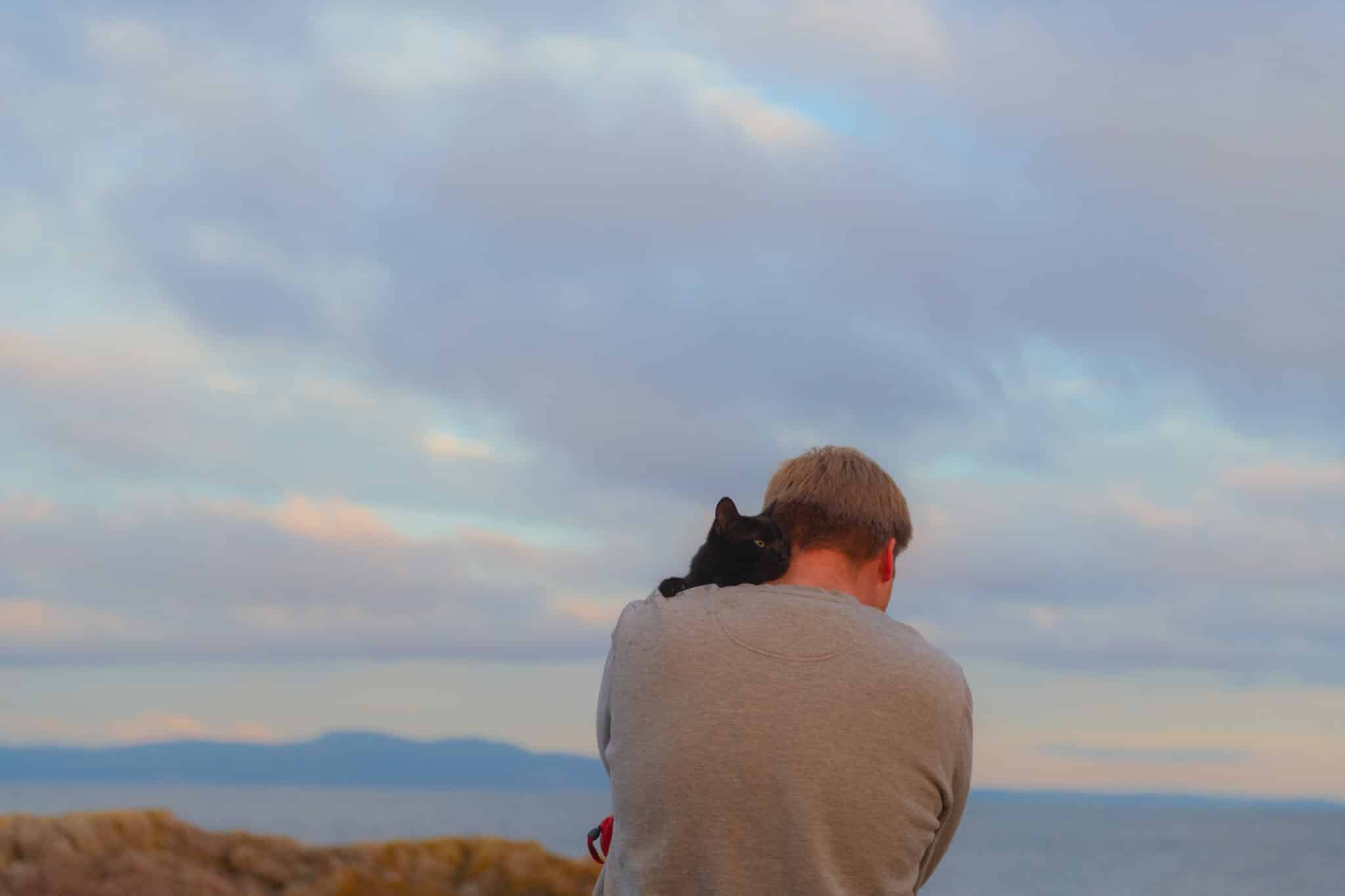 Man holds his black cat in a hug. The photo is very emotional